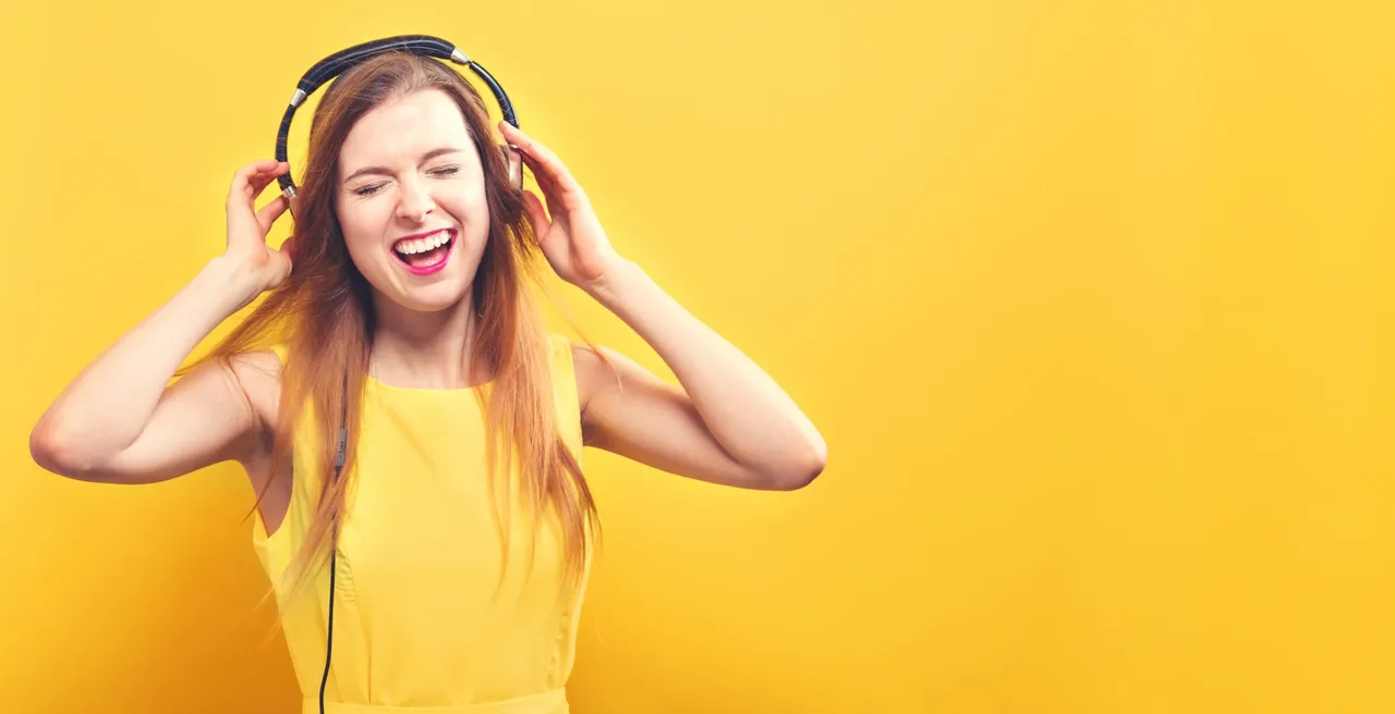 Young woman in yellow enjoying music with headphones against yellow background.