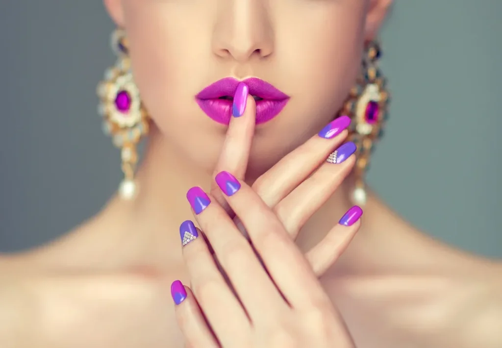 Close-up of a woman with vibrant purple lipstick and matching manicured nails.