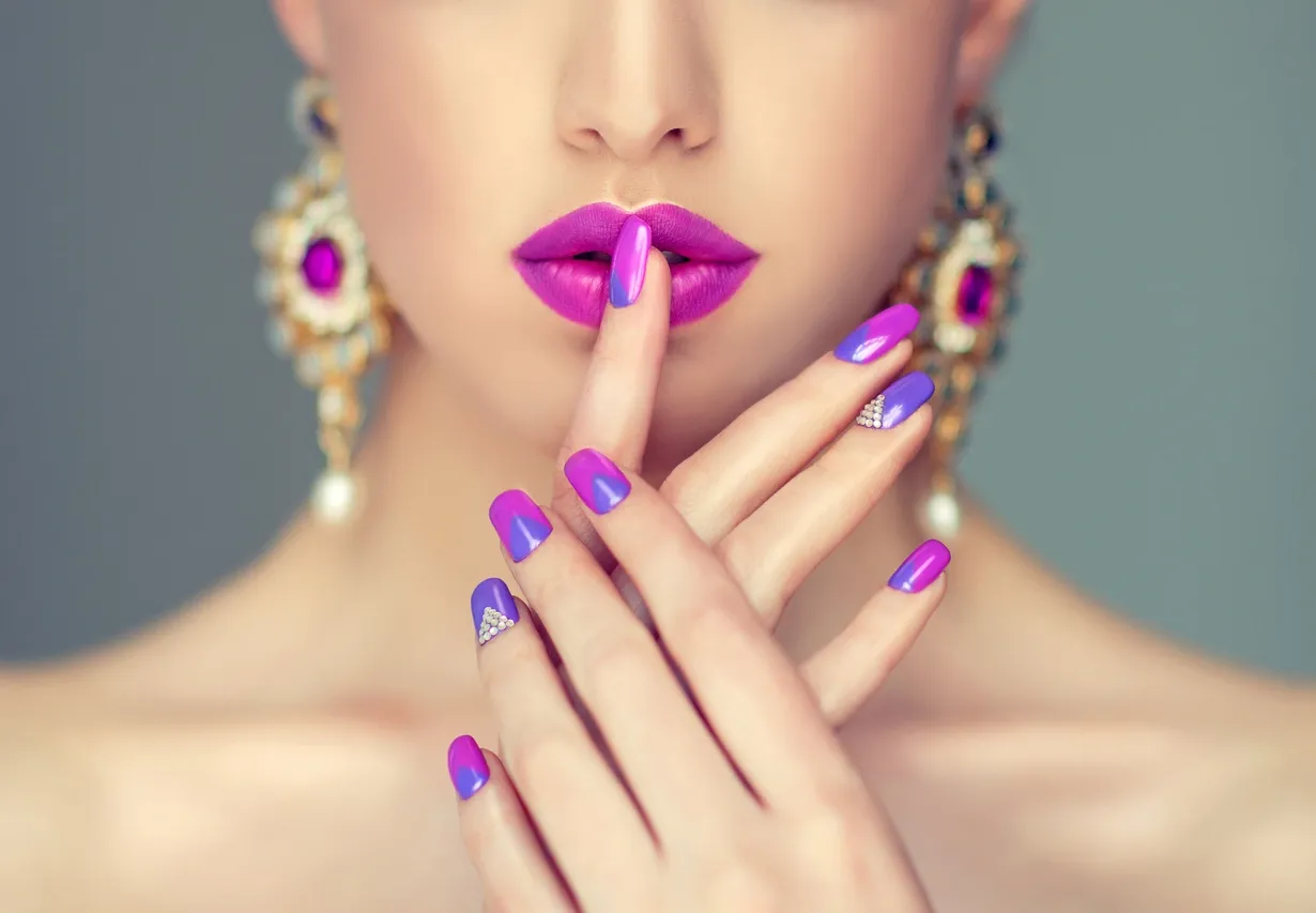 Close-up of a woman with vibrant purple lipstick and matching manicured nails.