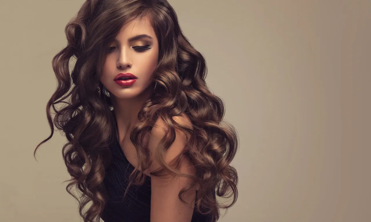 Woman with long, voluminous curly hair and a contemplative expression.