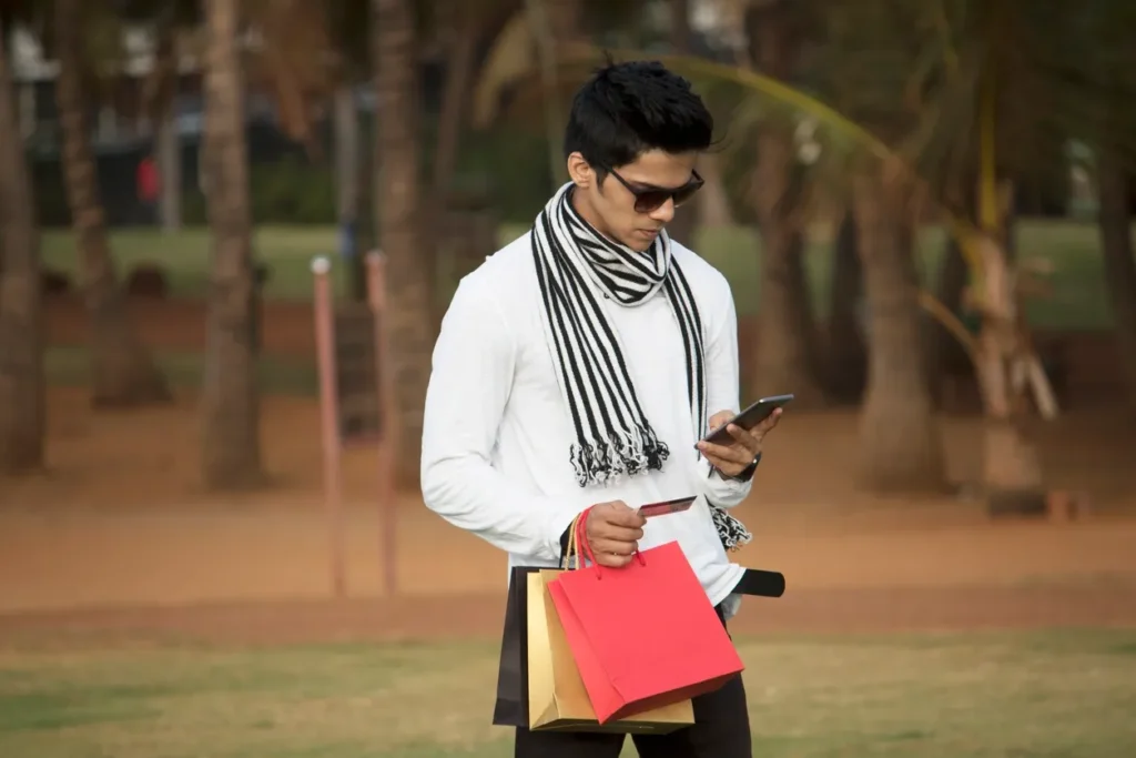 Man in white shirt holding colorful shopping bags and checking his phone.