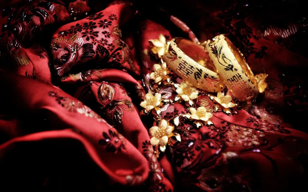 Two gold wedding rings on red embroidered fabric with decorative flowers.