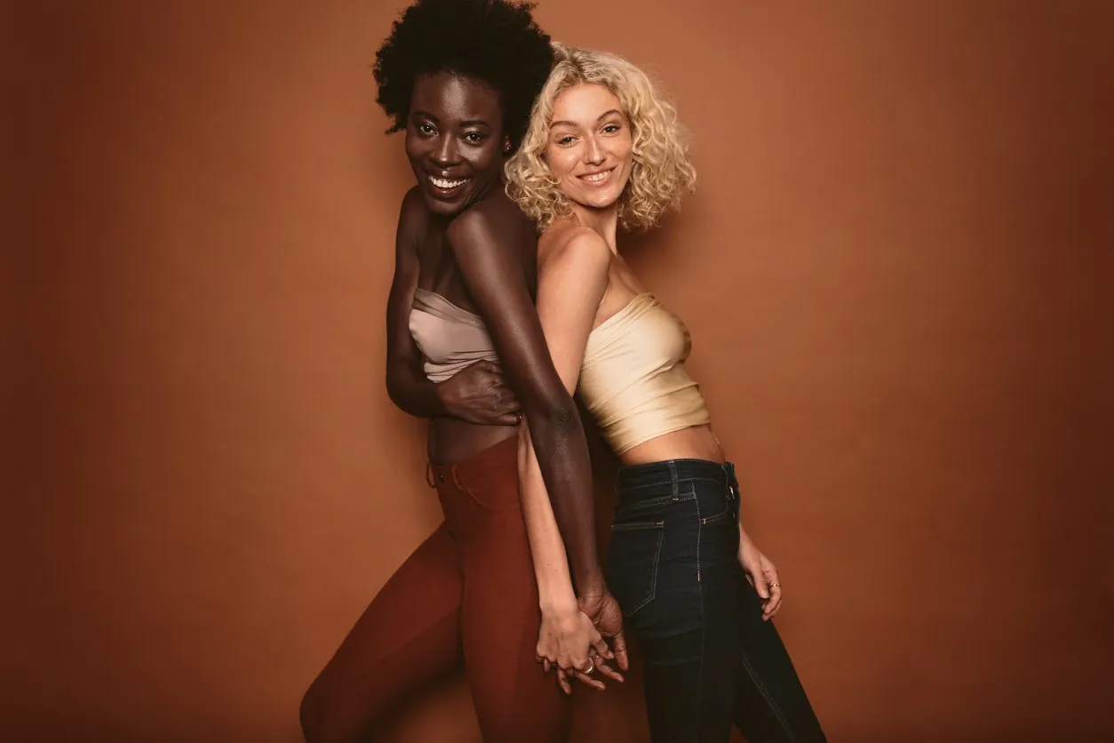 Two women smiling and holding hands against a brown background.