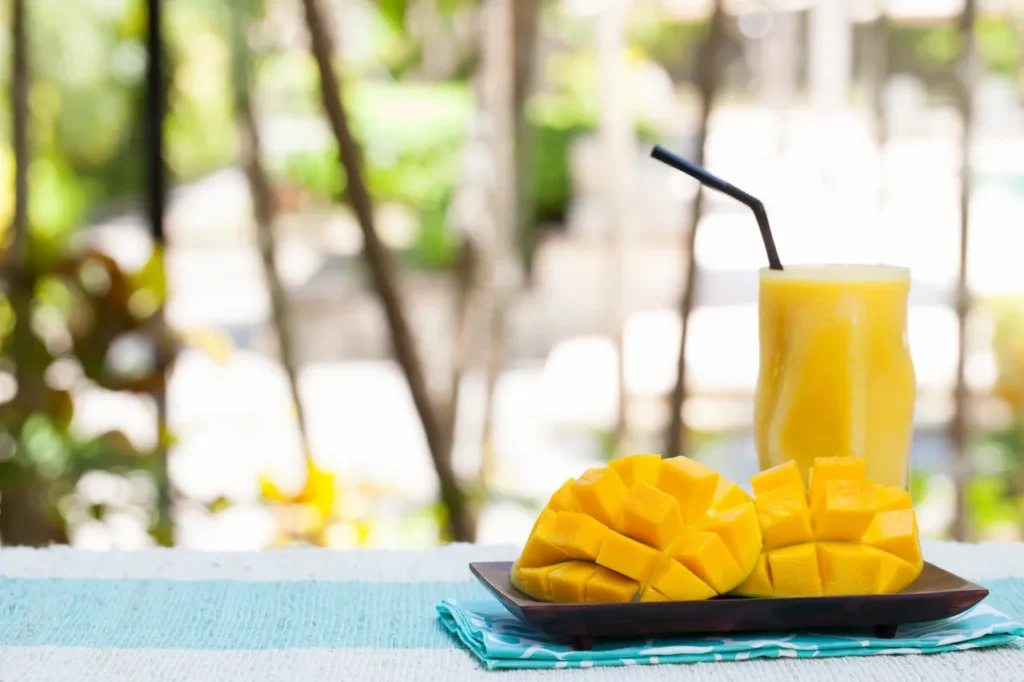 Fresh mango and mango juice on a table outdoors.