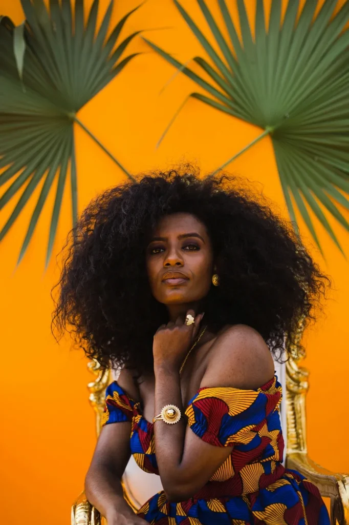 Woman with voluminous curly hair poses under a colorful umbrella.
