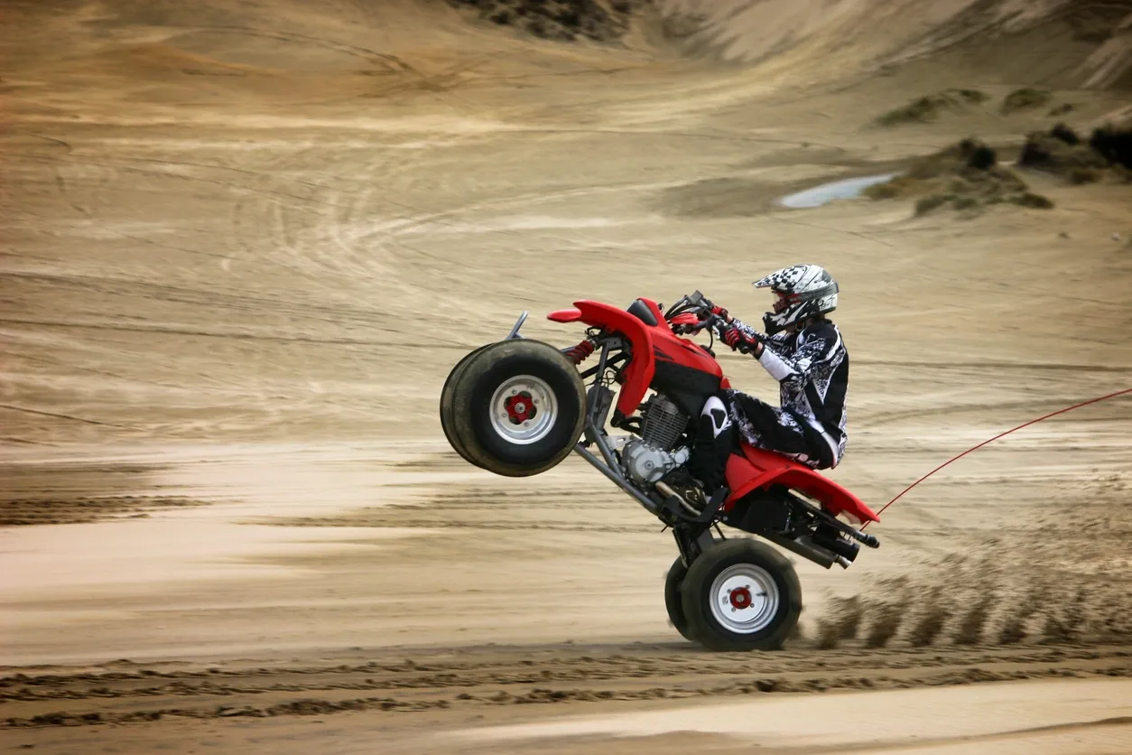 Person performing a wheelie on a red ATV in a sandy area.