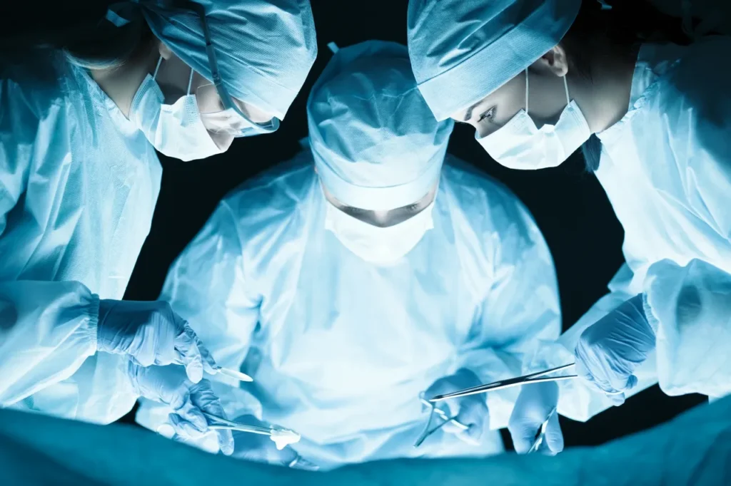 Surgeons in sterile gear performing an operation under bright lights.