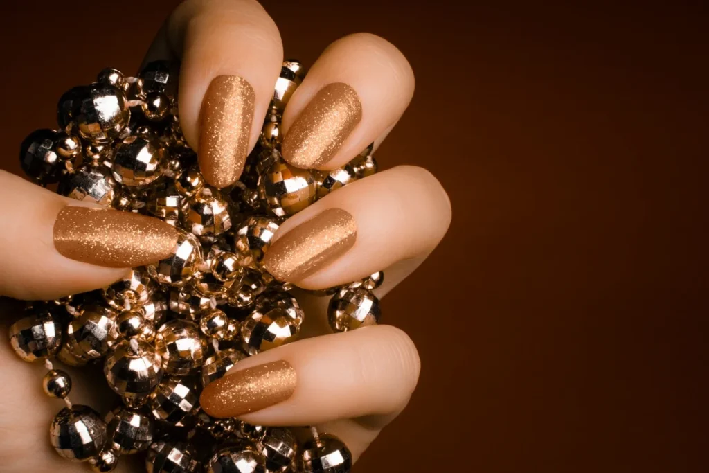 Shimmering gold nails holding a sparkling ornament.