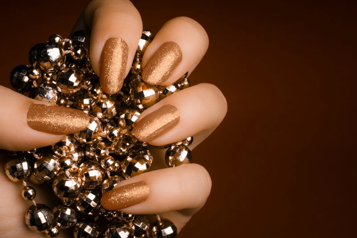 Shimmering gold nails holding a sparkling ornament.