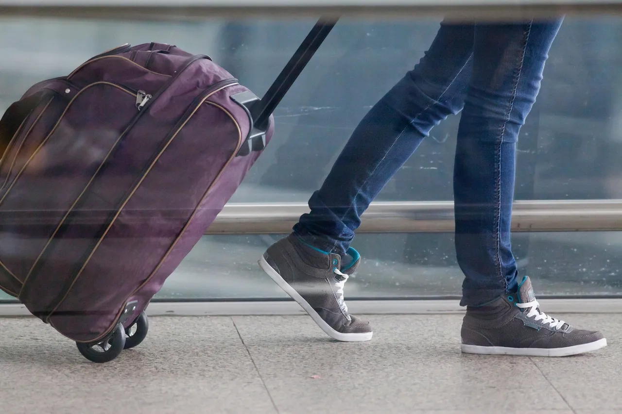 Traveler walking with a rolling suitcase in an airport.