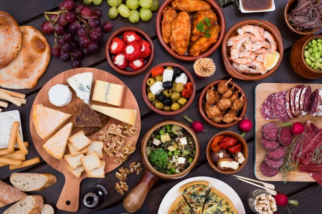 A colorful spread of cheeses, fruits, nuts, and appetizers on a wooden board.