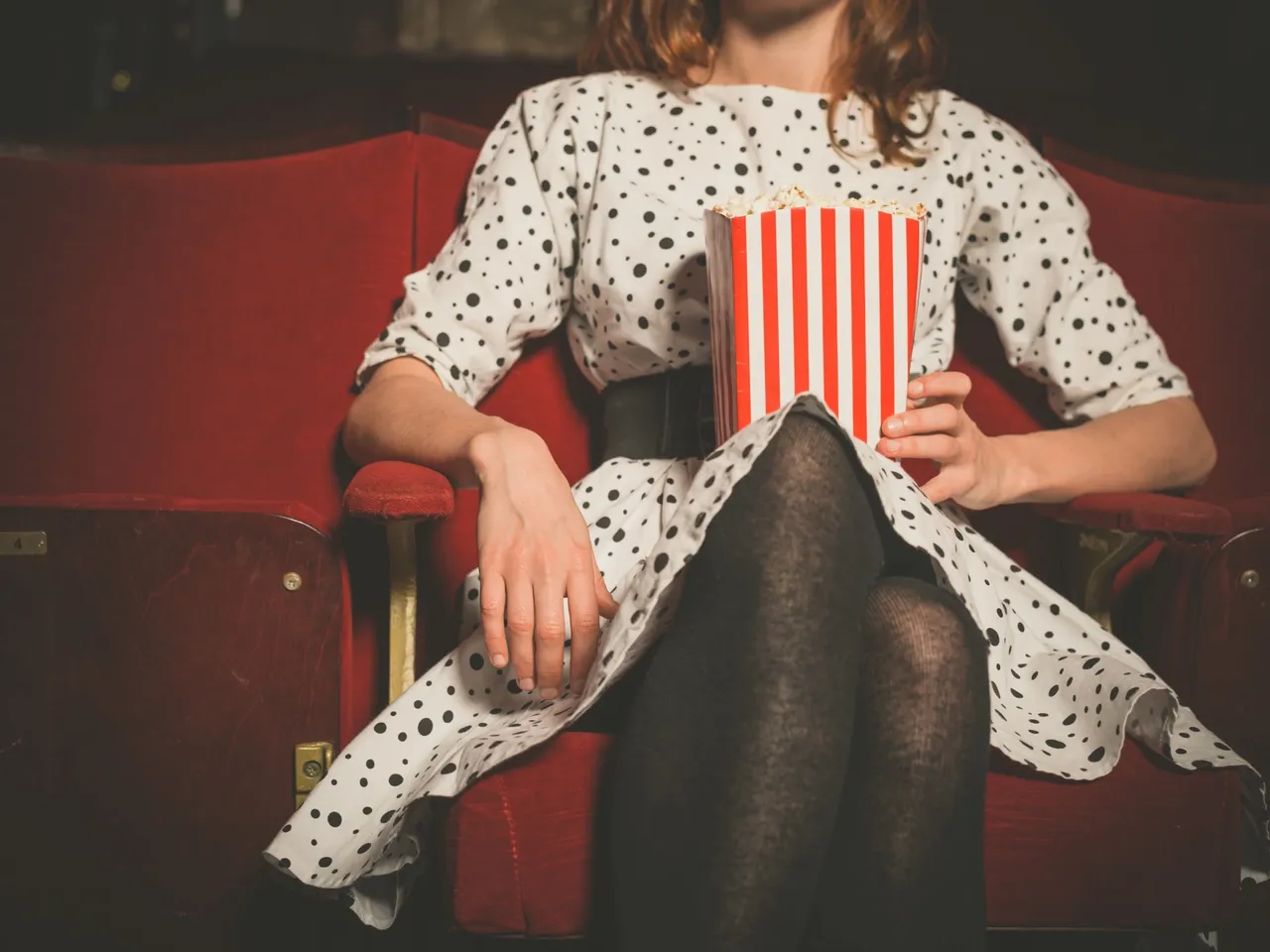 Person in polka dot dress holding popcorn at a theater.