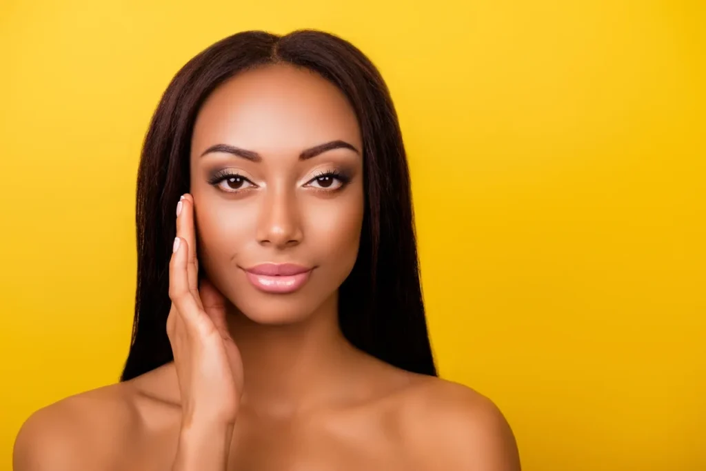 Portrait of a woman with flawless skin against a vibrant yellow background.