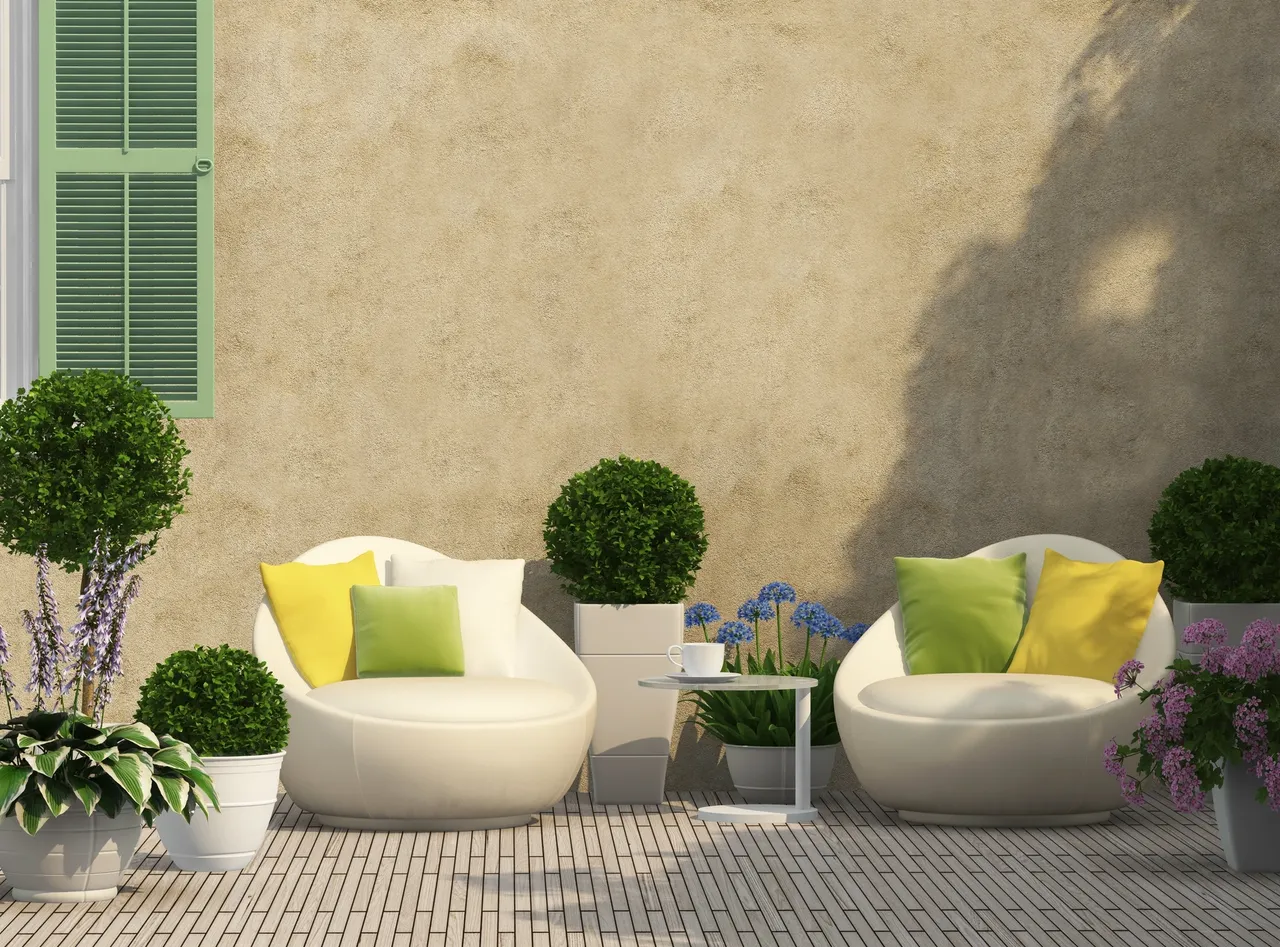Cozy outdoor seating with white cushioned chairs, green and yellow pillows, and small potted plants.