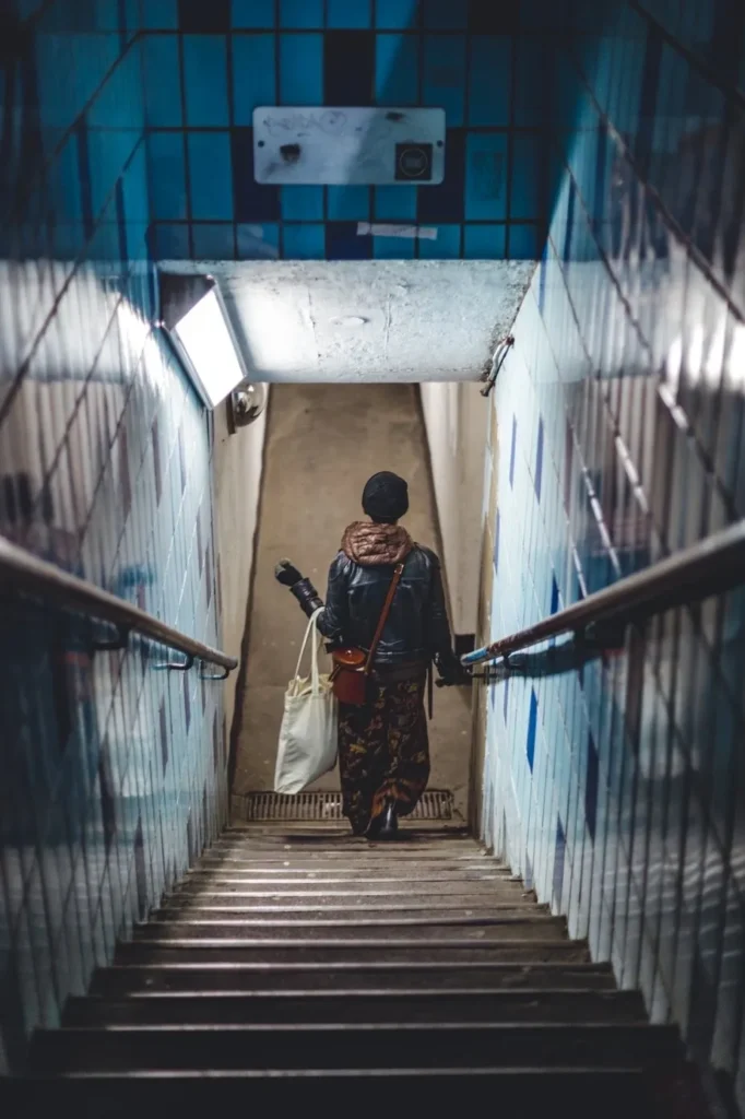 Person descending a dimly lit, narrow subway staircase.