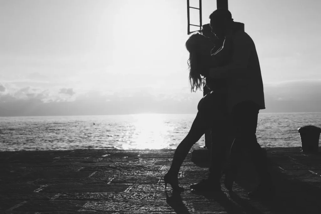Silhouette of a couple sharing a romantic moment by the sea at sunset.
