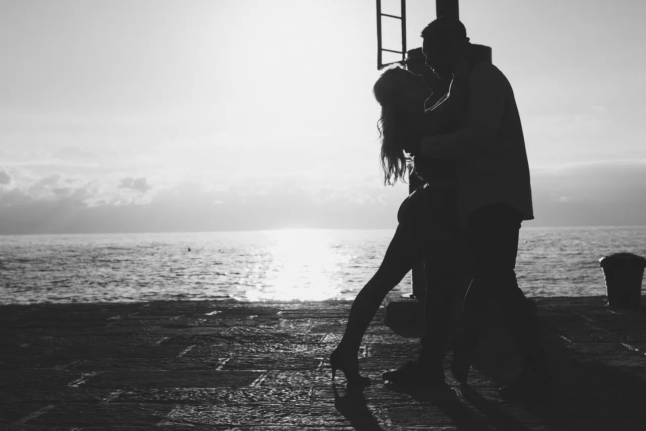 Silhouette of a couple sharing a romantic moment by the sea at sunset.