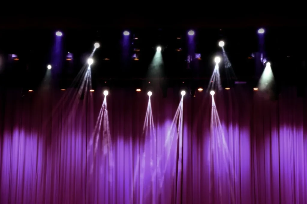 Stage lights shining down on a closed purple curtain.