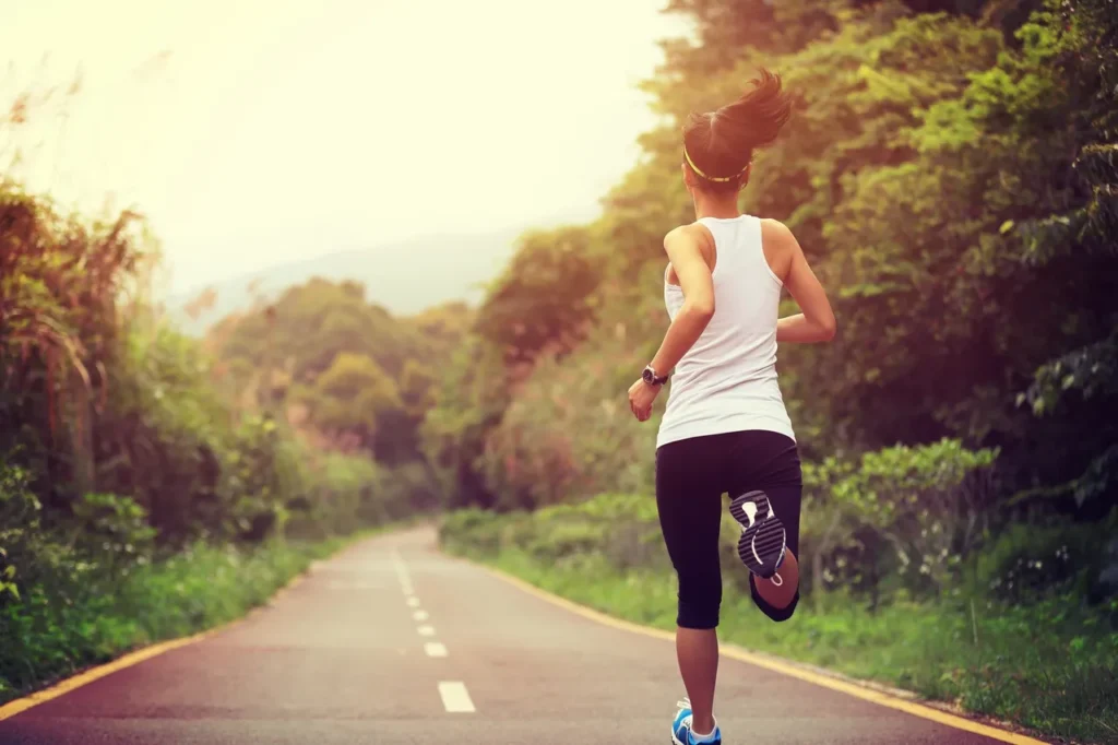 Woman jogging on a scenic road surrounded by greenery.