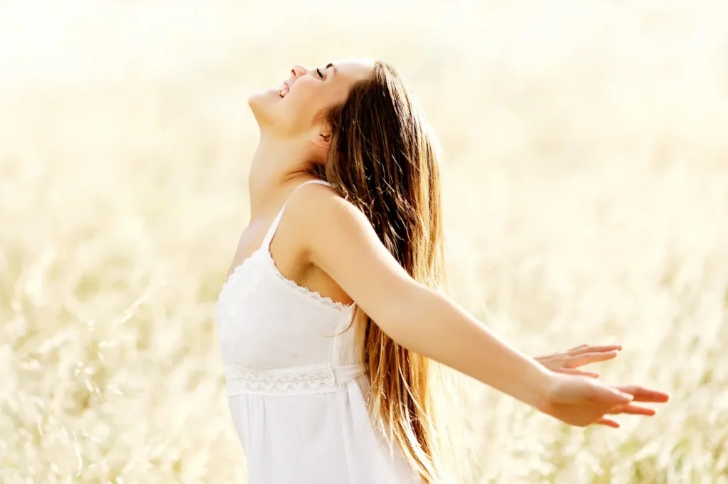 Woman in white dress enjoying freedom outdoors with arms outstretched.