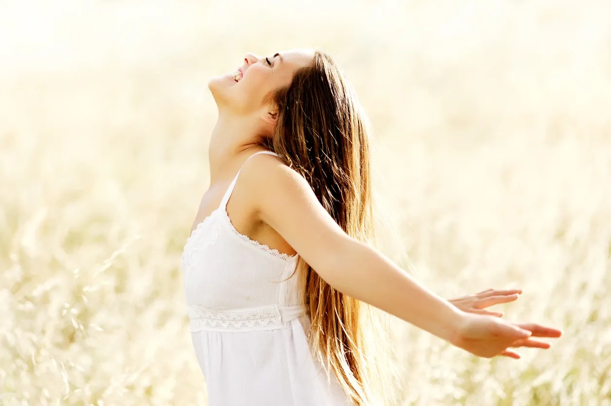 Woman in white dress enjoying freedom outdoors with arms outstretched.