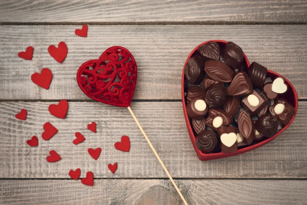 Heart-shaped chocolates and a decorative red heart on wooden surface.