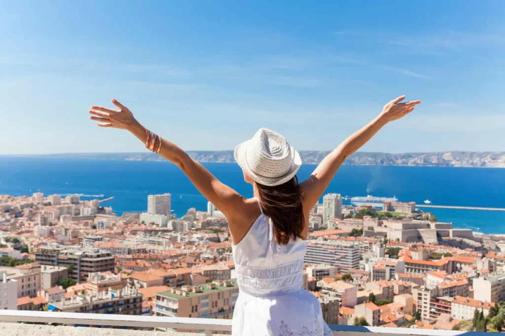 Woman in white enjoying city and ocean view with arms raised.