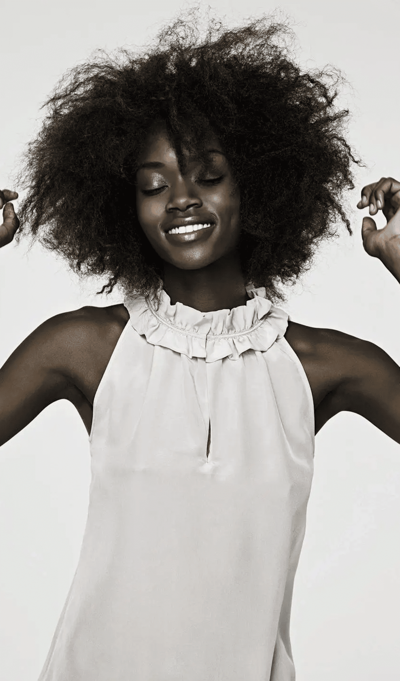Smiling woman dancing joyfully in a white sleeveless top.