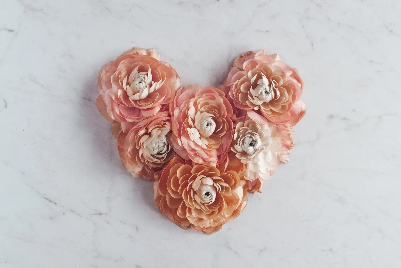 Heart shape made of peach-colored flowers with pearl centers on marble.