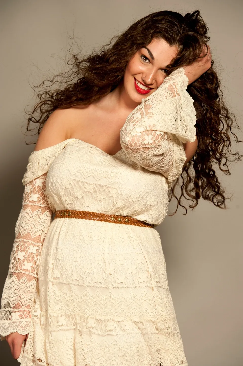 A woman in a white lace dress with long curly hair smiles.