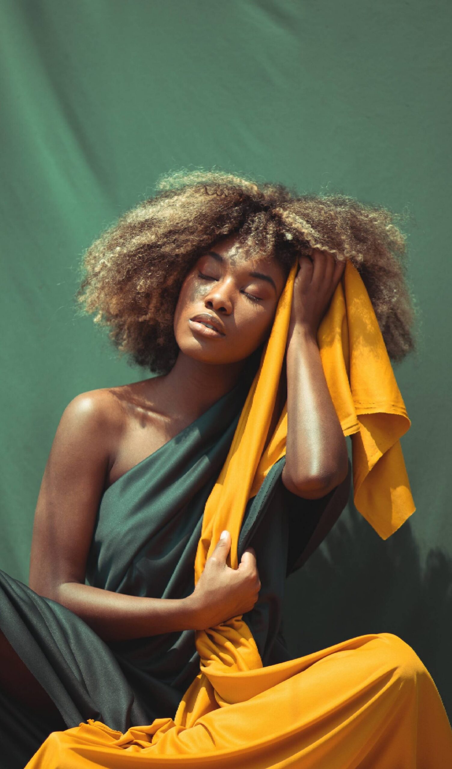 Person with afro holding yellow fabric, eyes closed